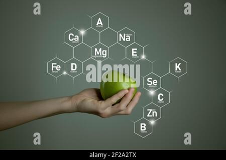 Frau`s Hand hält grünen Apfel, Mikroelement-Symbole in molekularen Sechsecken auf grauem Hintergrund. Gewichtsverlust Konzept Vorlage für Produktdesign. Stockfoto